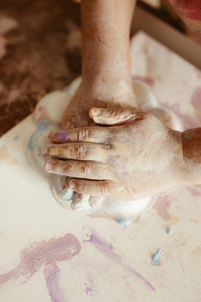 Hands covered in paint mixing colors on canvas